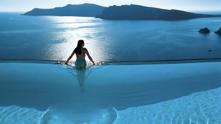 Woman standing at the edge of an infinity pool staring at the sea