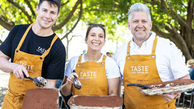 Three chefs in yellow aprons holding tiramisu