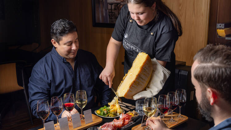 Chef shaving raclette cheese onto a diner's plate of food.