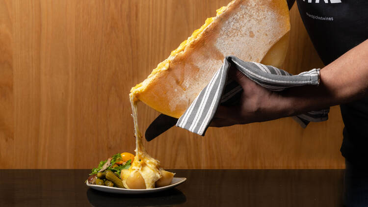Chef drizzling raclette cheese onto a plate of potatoes and other ingredients.