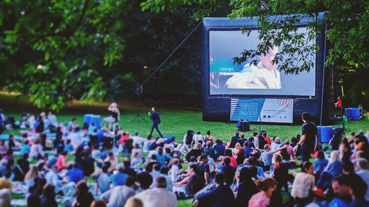 Films on The Green festival, people sit on the grass watching an inflatable screen.