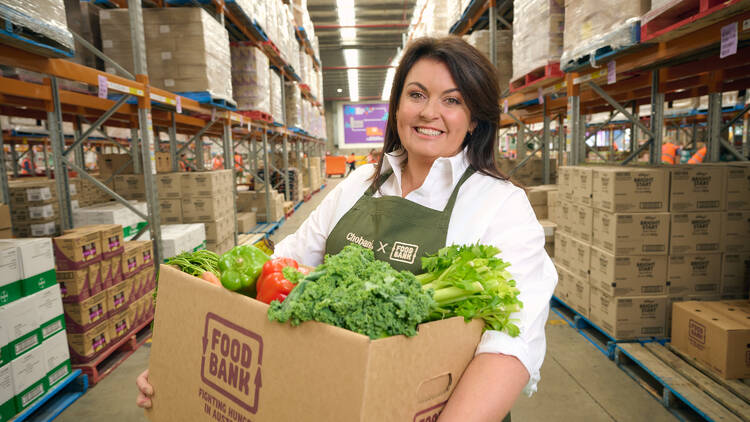 Chef Karen Martini holding a box of produce in a warehouse.