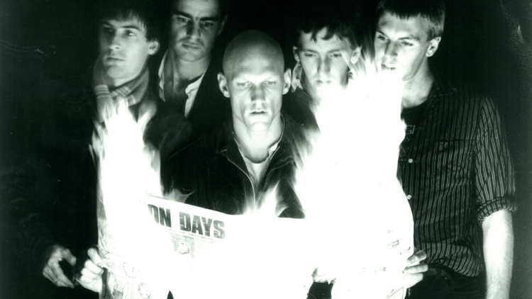 Peter Garrett and members of Midnight Oil stand around a burning newspaper