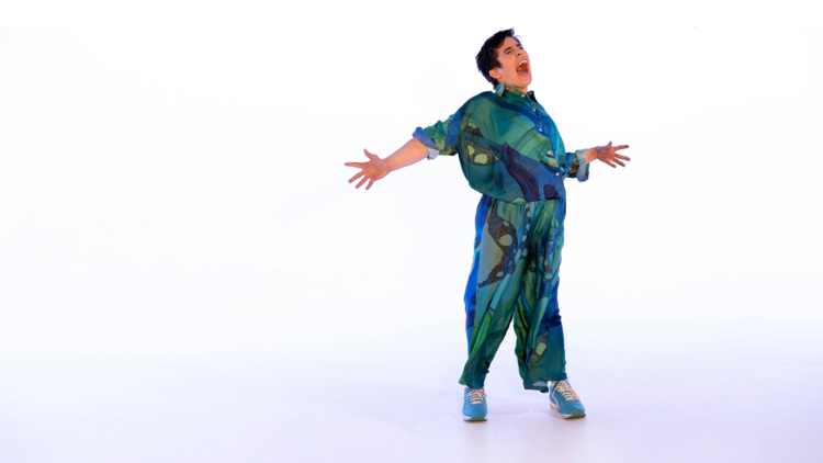 A person in a blue and green jumpsuit exclaiming with arms out