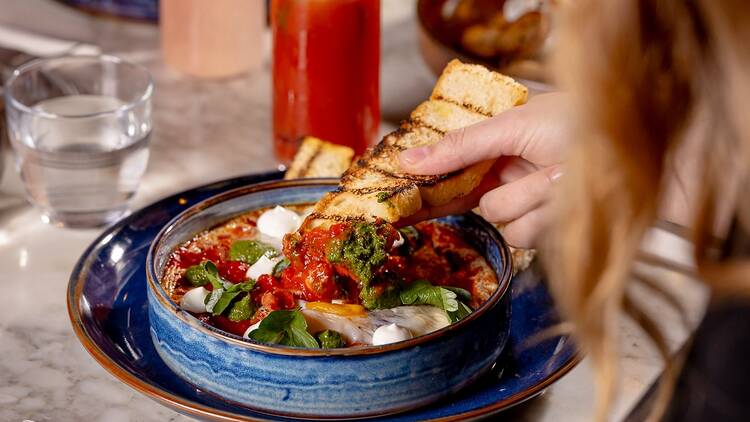 a person dips bread into a shakshuka dish 