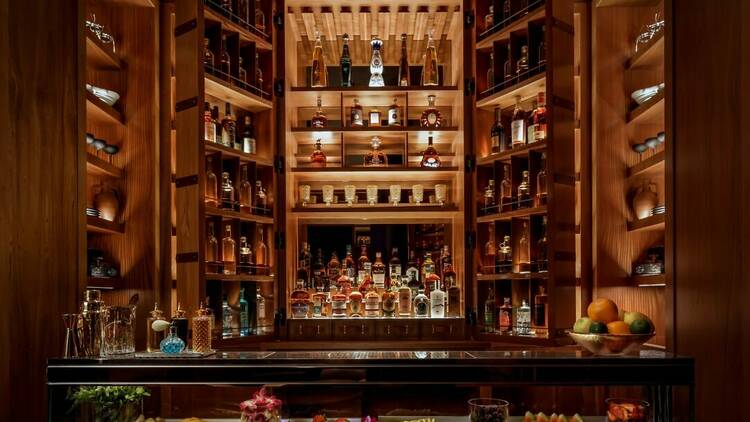 A glowing wood cabinet at speakesy bar Old Wives' Tale is open to show a variety of bottles and colorful fruit