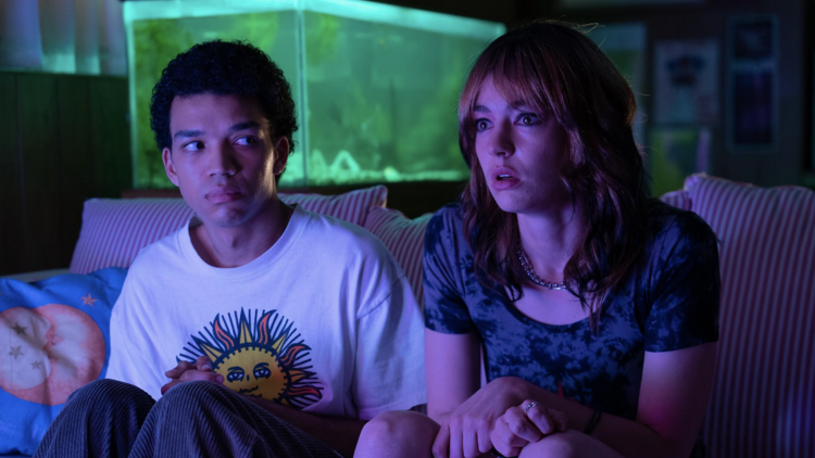 Two young people sitting on a couch bathed in a purple light