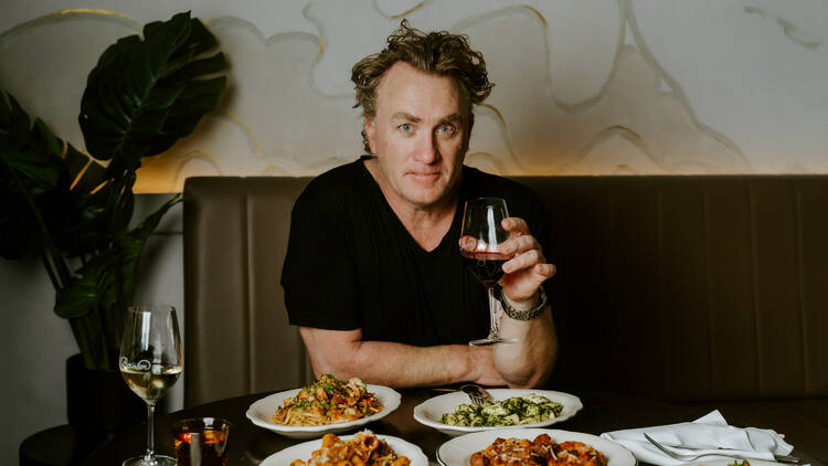 Adrian Richardson with a glass of wine and plates of pasta.