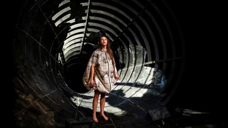 Carly Sheppard wears a globe-esque costume and stands on the edge of a grey funnel