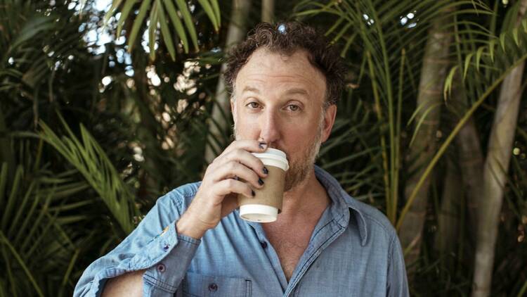 Lead singer of the band Guster, Ryan Miller sips from a paper cup of coffee and looks at the camera