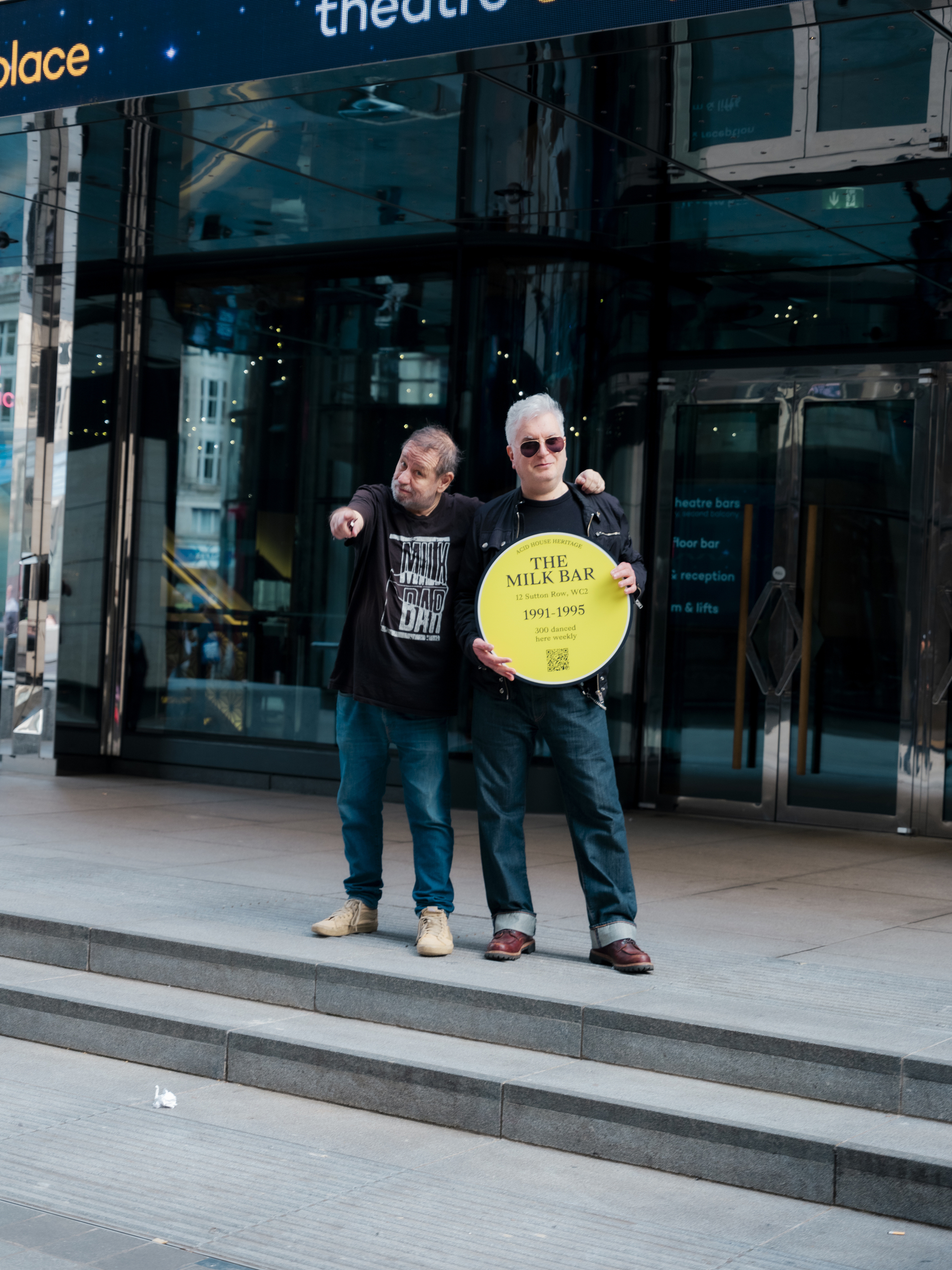 Two men stood outside a music venue holding a yellow plaque