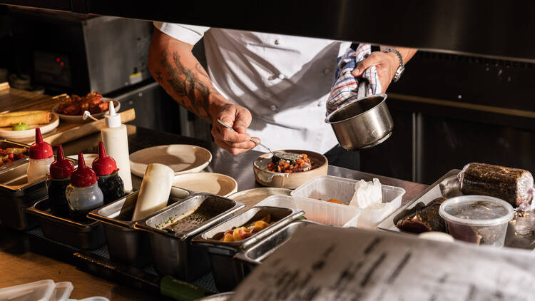 A chef pouring sauce over a dish in a kitchen.