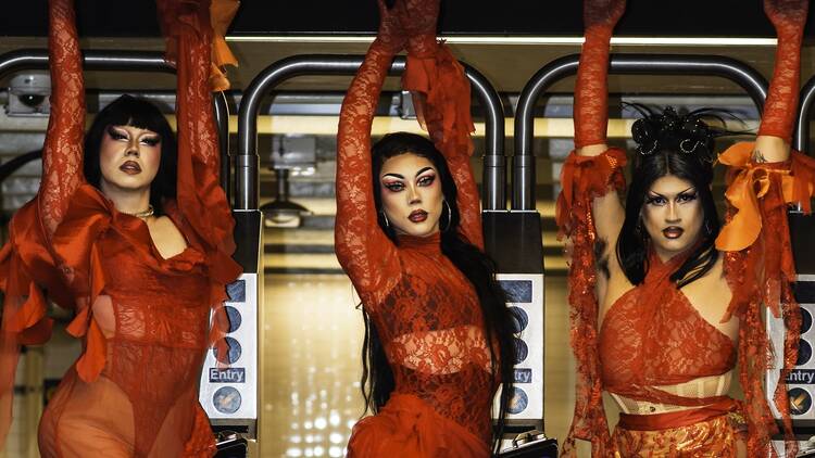 three drag queens wearing all red hanging on a subway entrance