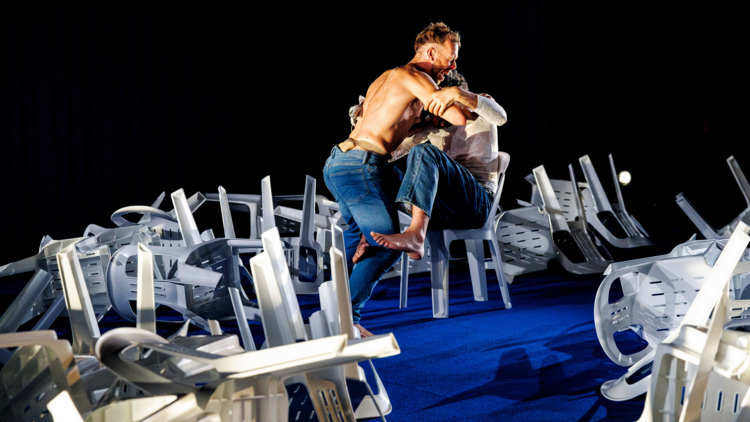 Two men embrace in a mess of chairs
