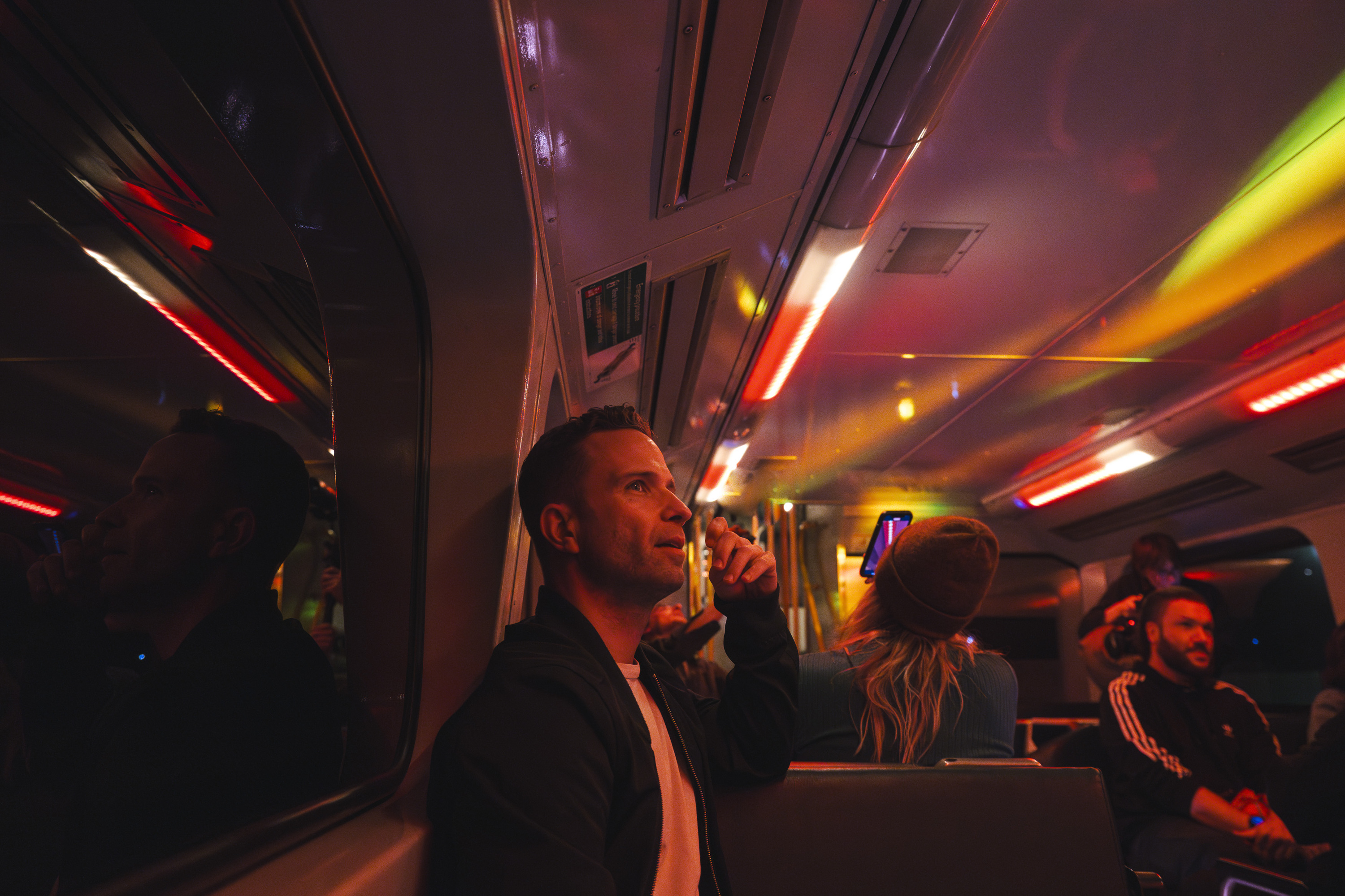 A man sitting on a train lit with cool looking red and yellow lights.