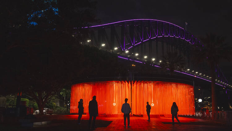 The Sydney Harbour Bridge lit up for Vivid, with a red light installation underneath.