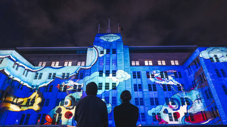 People looking up at the MCA lit up in the dark at Vivid 2024.
