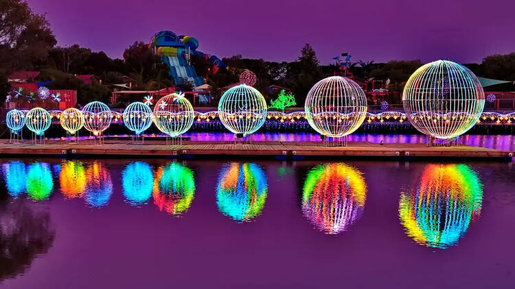 A lake with colourful circular light installations reflected in the water.