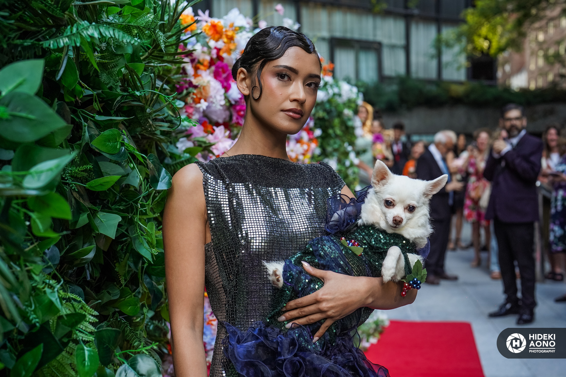 A model holds a dog dressed up in a blue dress.