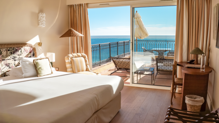 Deluxe suite with a cream colour scheme, large bed and a large balcony facing the sea.