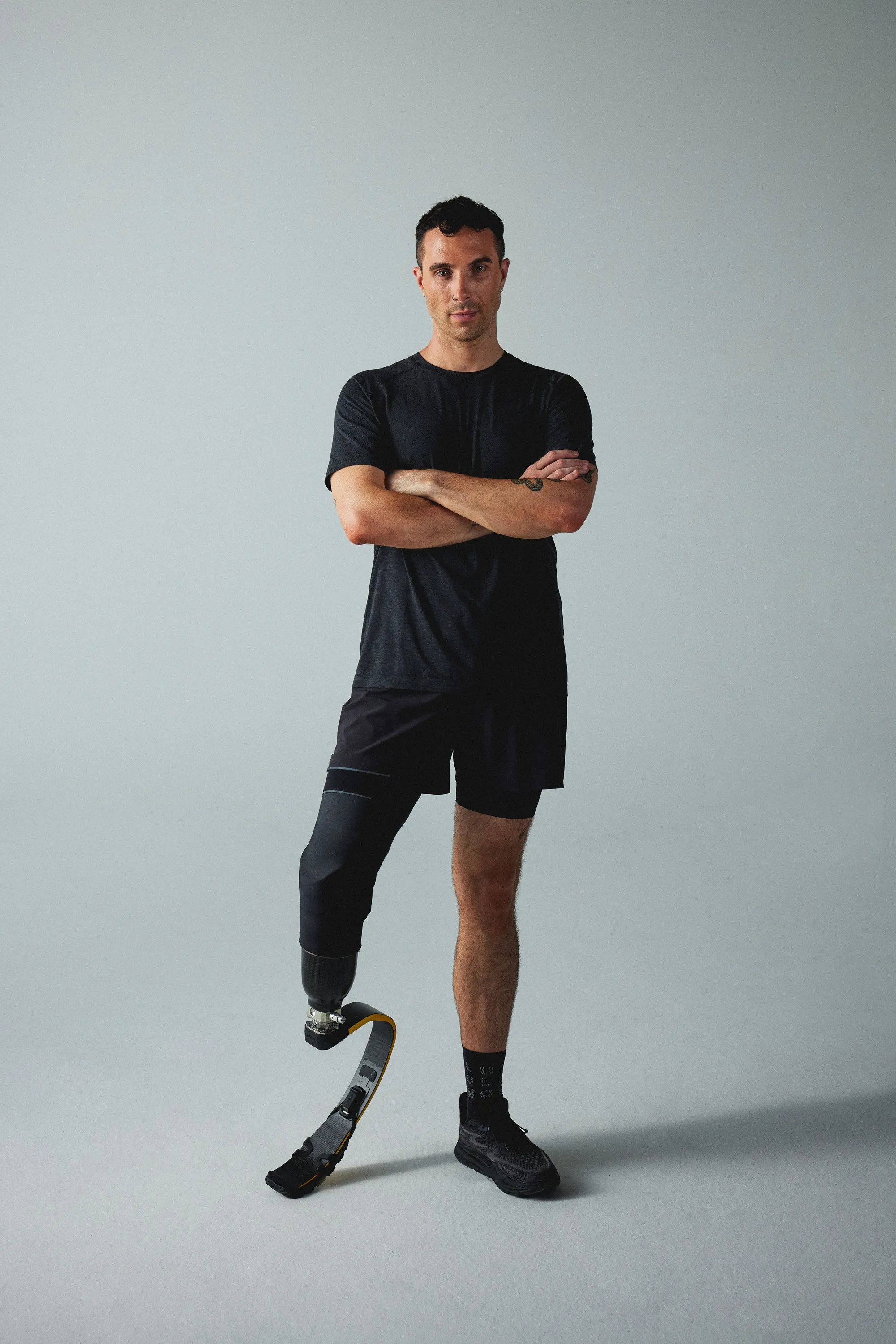 James Parr, standing wearing a black t-shirt and shorts, with crossed arms. He has a one prosthetic leg.