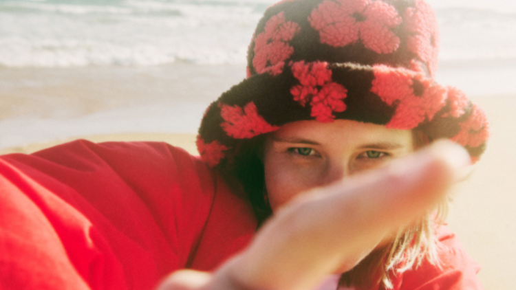 Alice Ivy stands on the beach in a black and red floral fluffy bucket hat