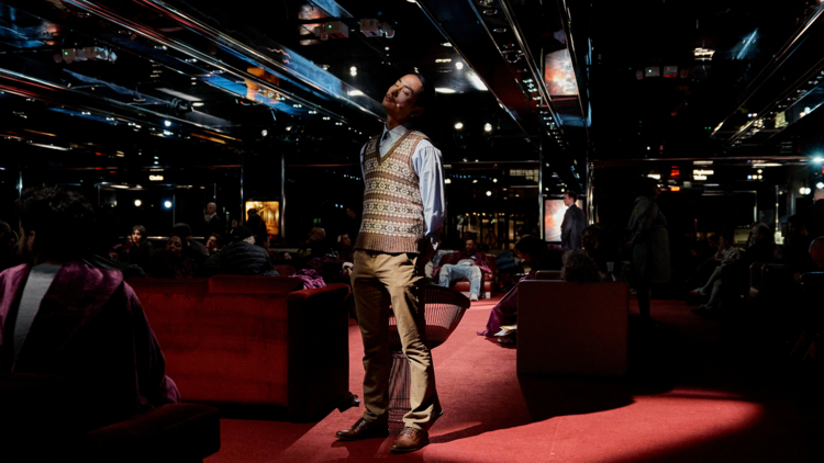 Performer stands in the arts centre foyer surrounded by people resting on couches