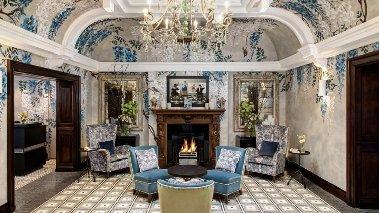 Drawing room with four armchairs and a fireplace and a chandelier at Brown's Hotel.