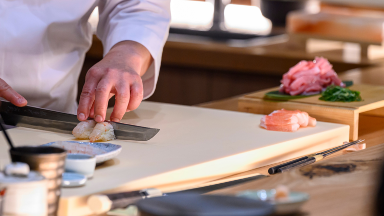 Chef preparing sushi with a knife.