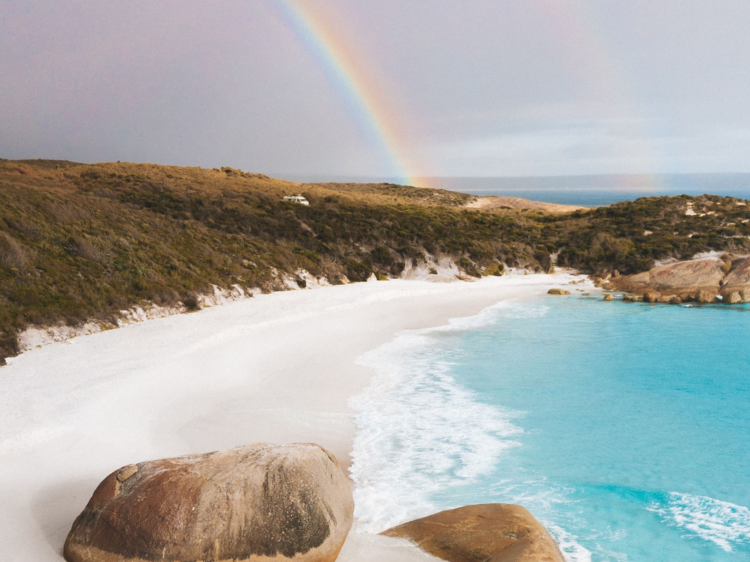 A white beach and blue water with rainbow