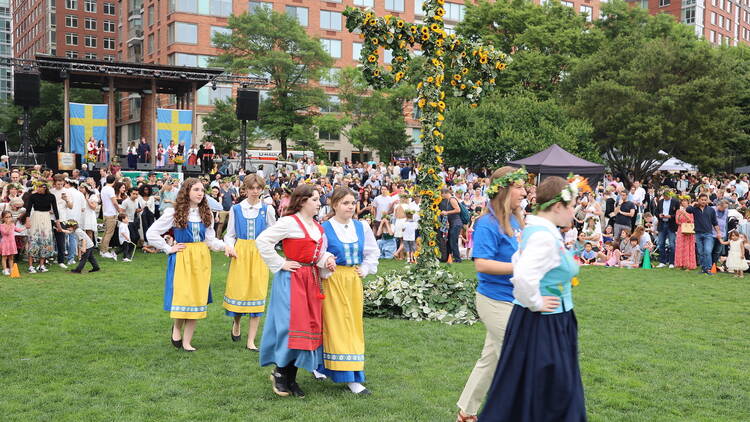 People in traditional Scandinavian dress walk by a Maypole.