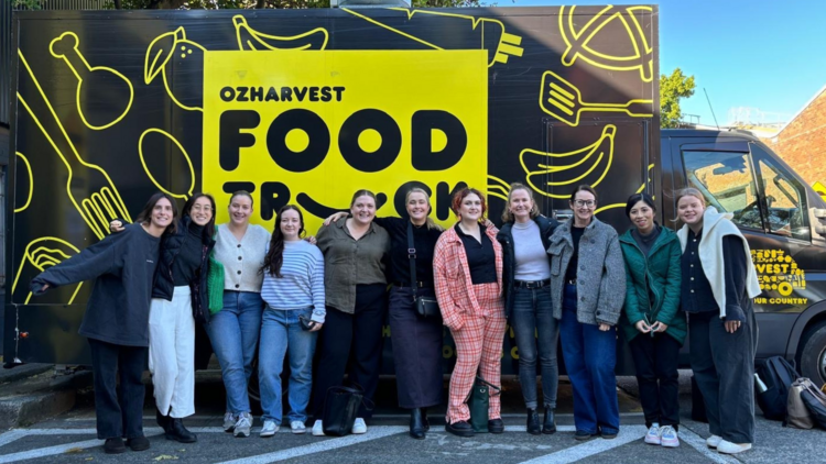 Team posing in front of OzHarvest's black and yellow food truck