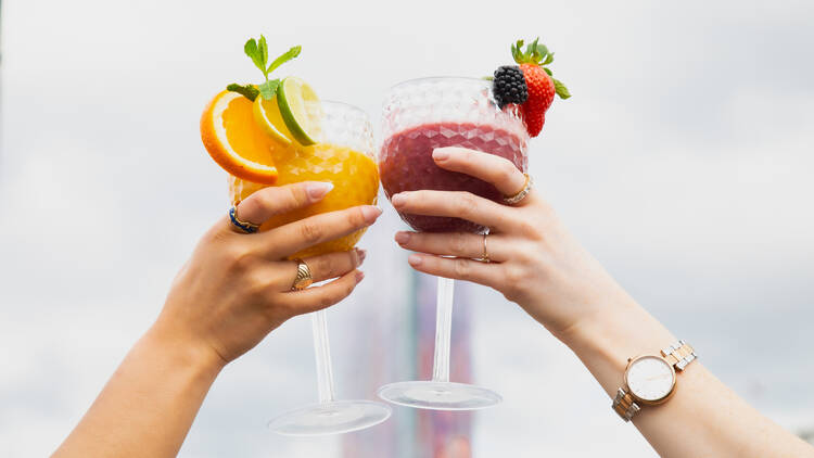 Two hands holding up colourful fruity cocktails 