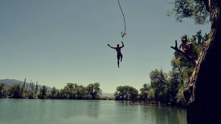 Man jumping into lake from rope