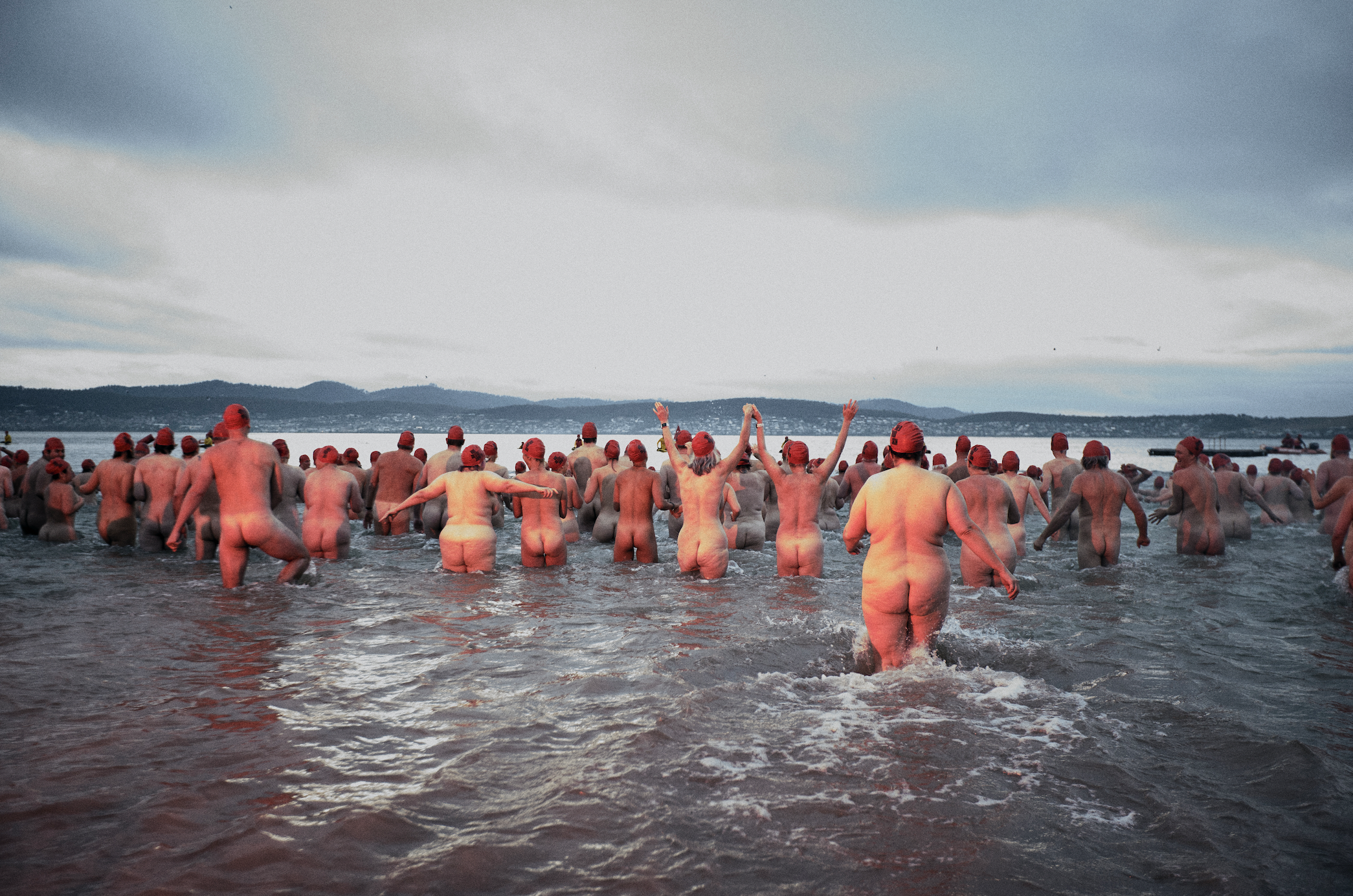 People running naked into the water wearing red caps