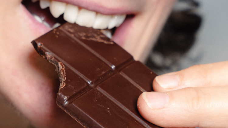 Woman biting into a block of chocolate.