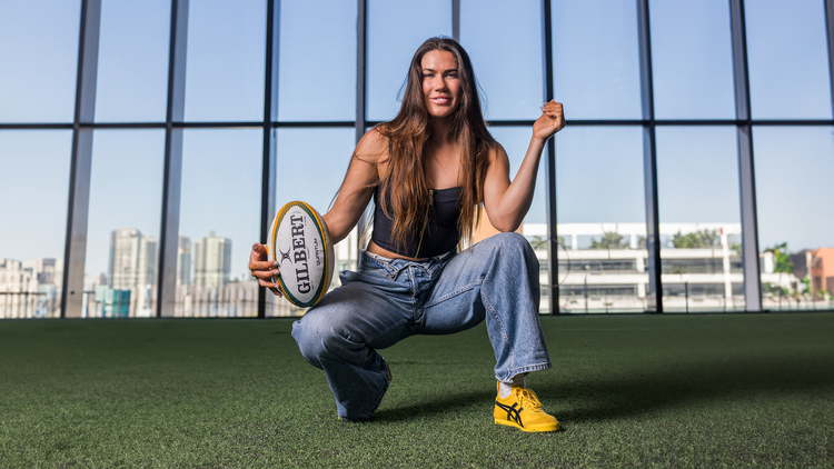 Football player Charlotte Caslick kneeling down and holding a football.