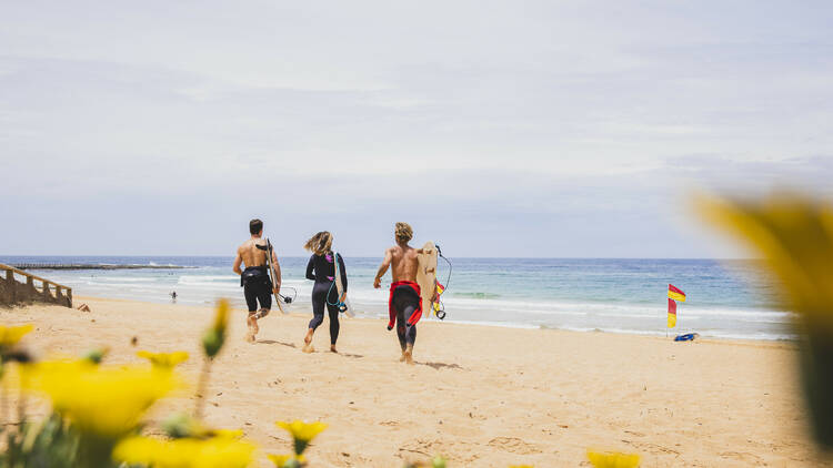 Surfers heading into the waves at North Narrabeen Beach, North Narrabeen on Sydney's northern beaches.