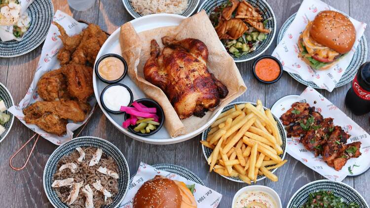 Chicken, chips, pickles, salad, rice and burgers on a table.