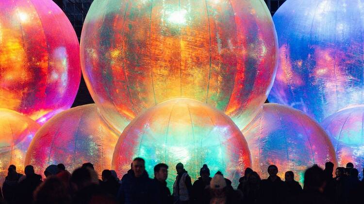 A crowd of people stand around giant colourful bubbles. 