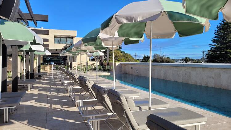 A pool with white-and-mint-coloured umbrellas above sun lounges