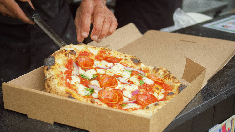Image of Neapolitan style, pepperoni pizza being lifted out of its box by the pizza vendor