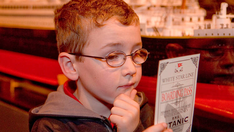 A child reads a boarding pass for Titanic: The Artifact Exhibition 