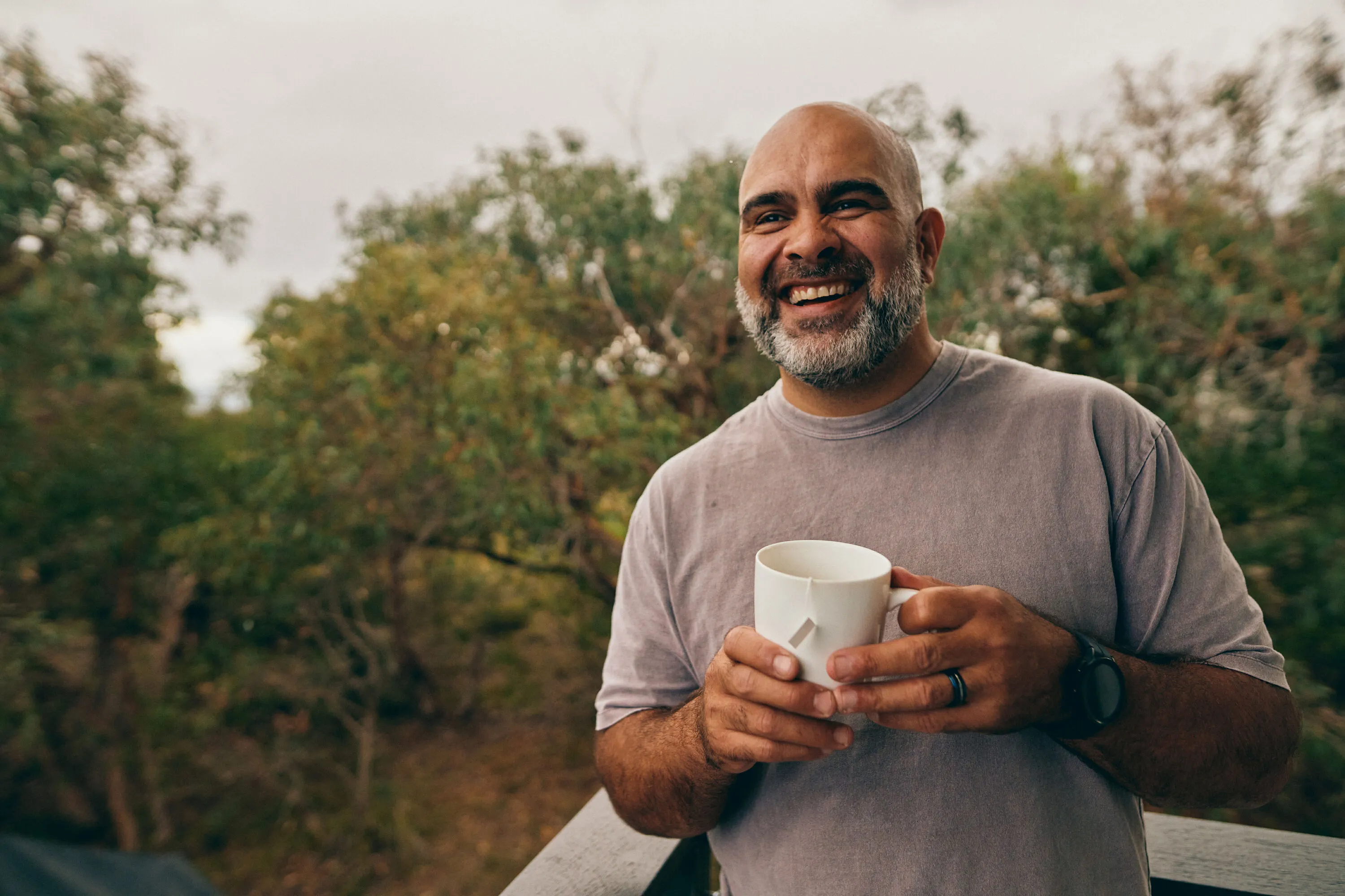 Troy Benjamin smiling outdoors with a mug of Blak Brews tea.