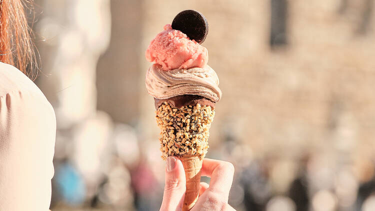 picture of a hand holding an ice cream with strawberry and chocolate scoops 