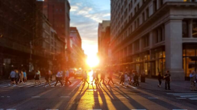 People cross busy intersection on 23rd Street in Manhattan New York City with the colorful light of sunset casting long shadows