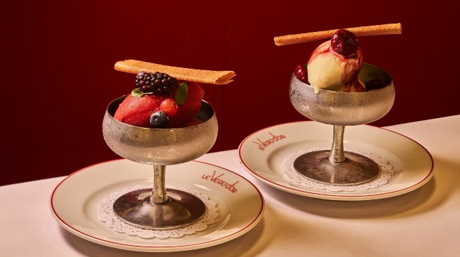 Two silver cups filled with ice cream, one white scoop and one red, are sitting on a white tableclothed table. 