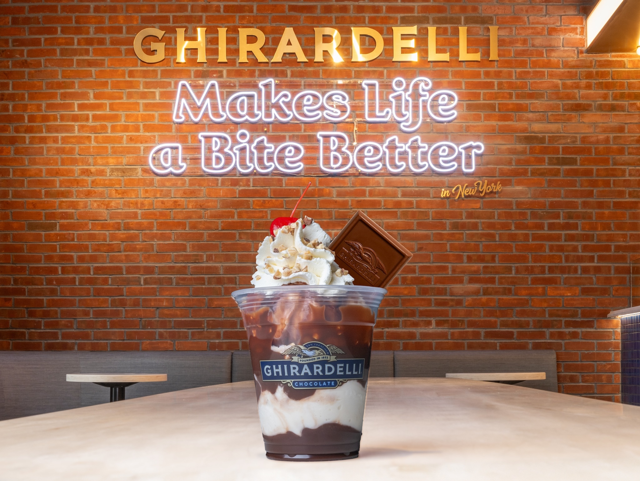 An ice cream sundae in front of a sign reading Ghirardelli Makes Life a Bite Better.