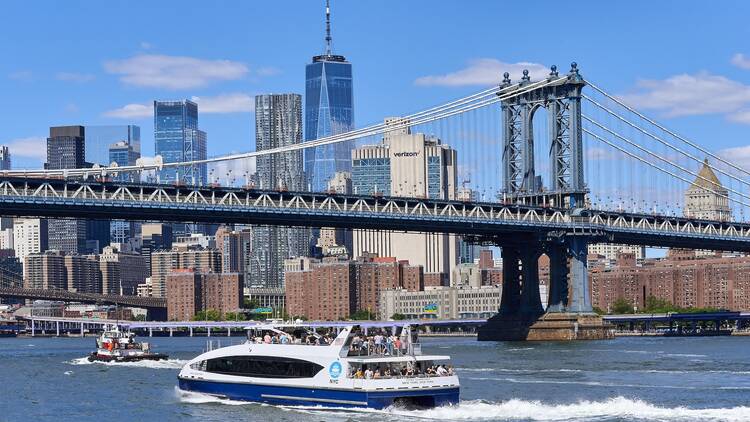 New York, NY - August 13, 2022: A crowded NYC Ferry travels on the East River, Behind is the Manhattan Bridge and the skyscrapers of Lower Manhattan on a clear summer day.