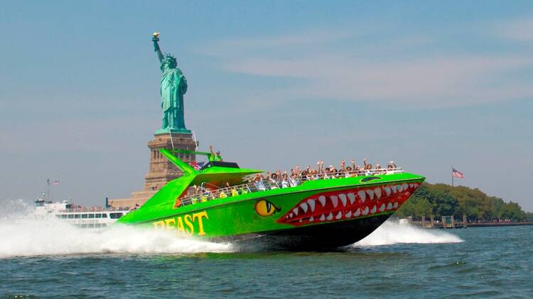 A green boat called The Beast in front of the Statue of Liberty.